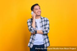 Happy Asian male talking on phone in studio shoot with arm over his chest bYxyX4