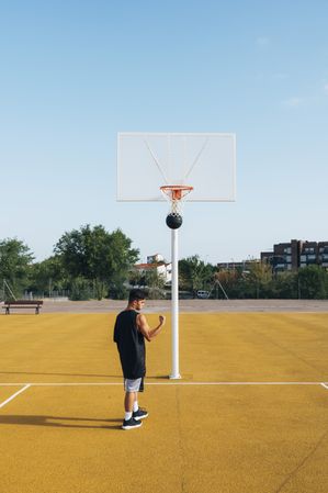 Young man playing on yellow basketball court outdoor.
