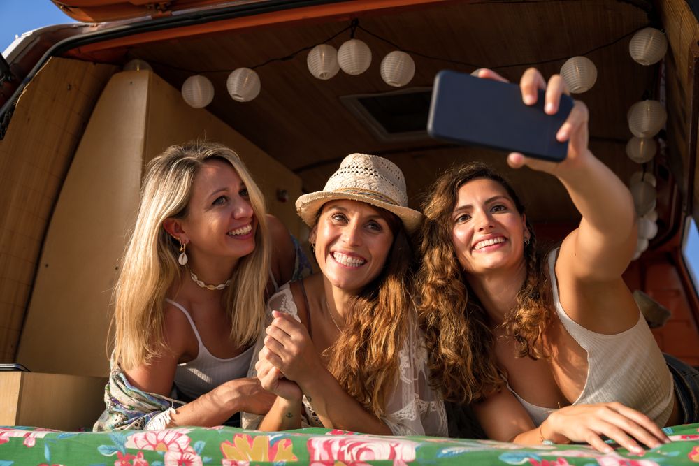 Relaxed female friends taking selfie comfortable placing on trunk of blue car
