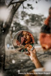 Woman in brown scarf holding round mirror 5kMZob