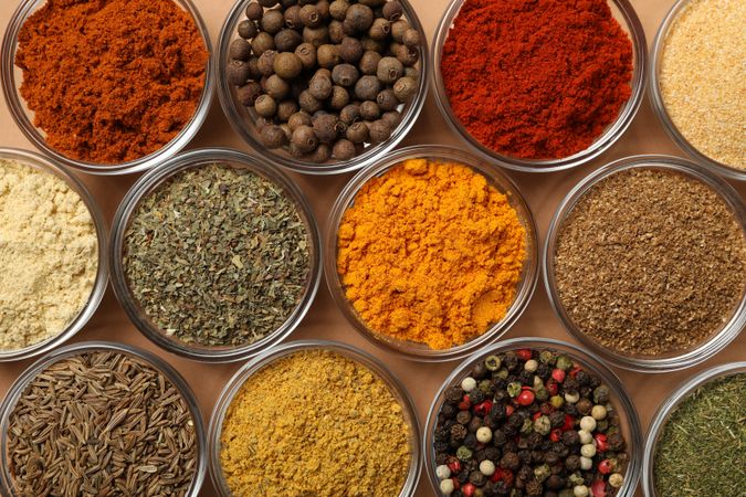 Top view of glass bowls of spices in rows on beige table