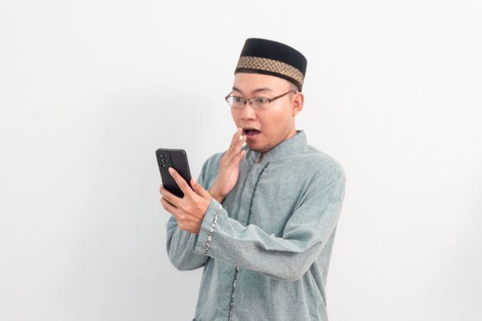 Surprised Asian Muslim man holding phone in Ramadan