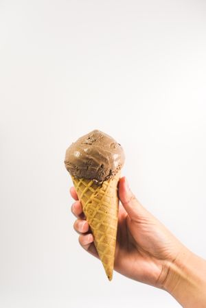 Hand holding chocolate ice cream cone, vertical