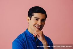 Hispanic man smiling at camera in pink studio with hand on chin 0L7Jrb