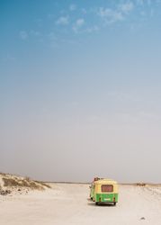 Colorful minibus with trailer parked on sandy shore in sunny day