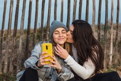 Young woman kissing cheek of girlfriend while resting together on boardwalk in nature
