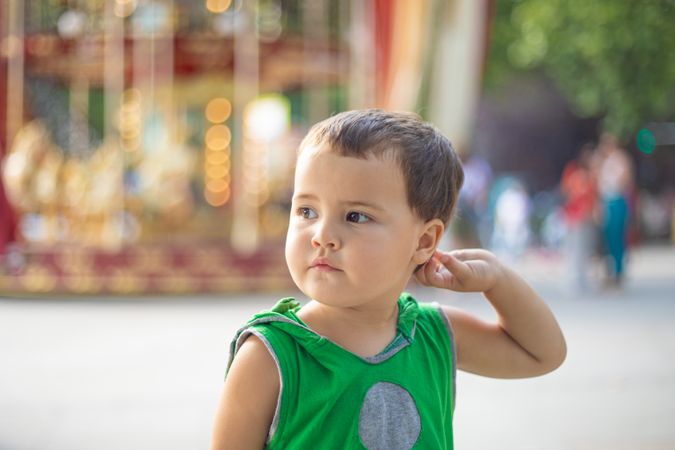 Child standing near moving carousel and dreaming at fair