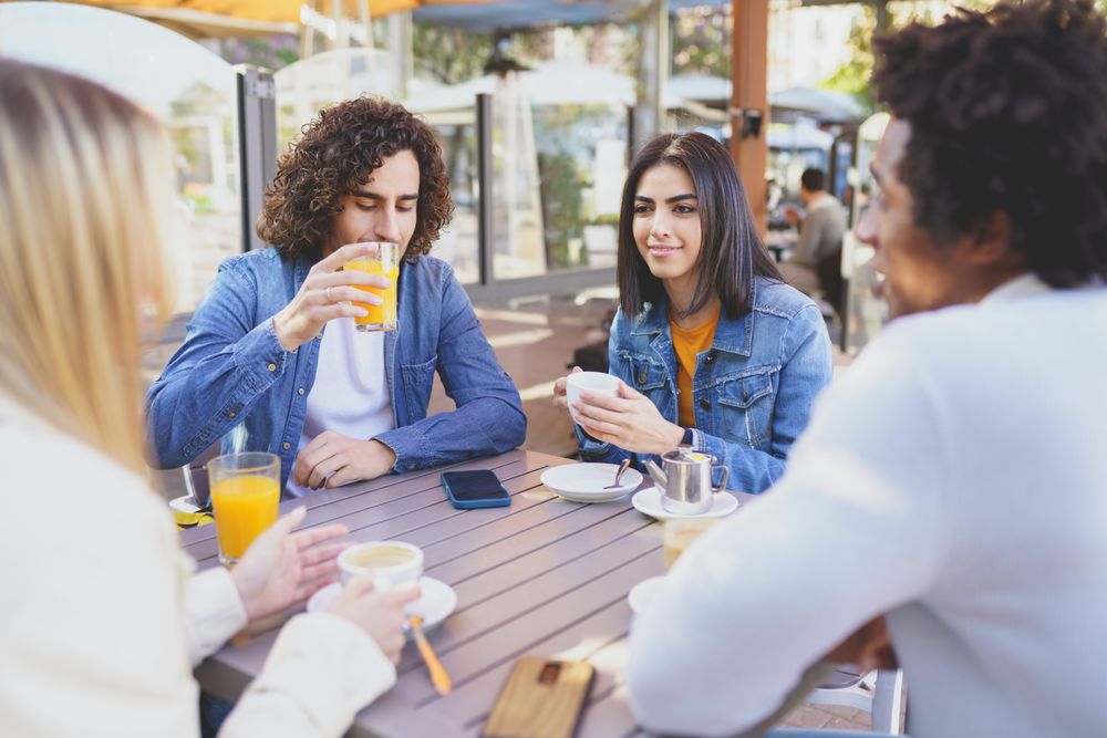 Group of friends meeting up over coffee and juice at outside table