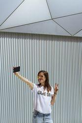 Cheerful woman taking selfie and posing near modern wall