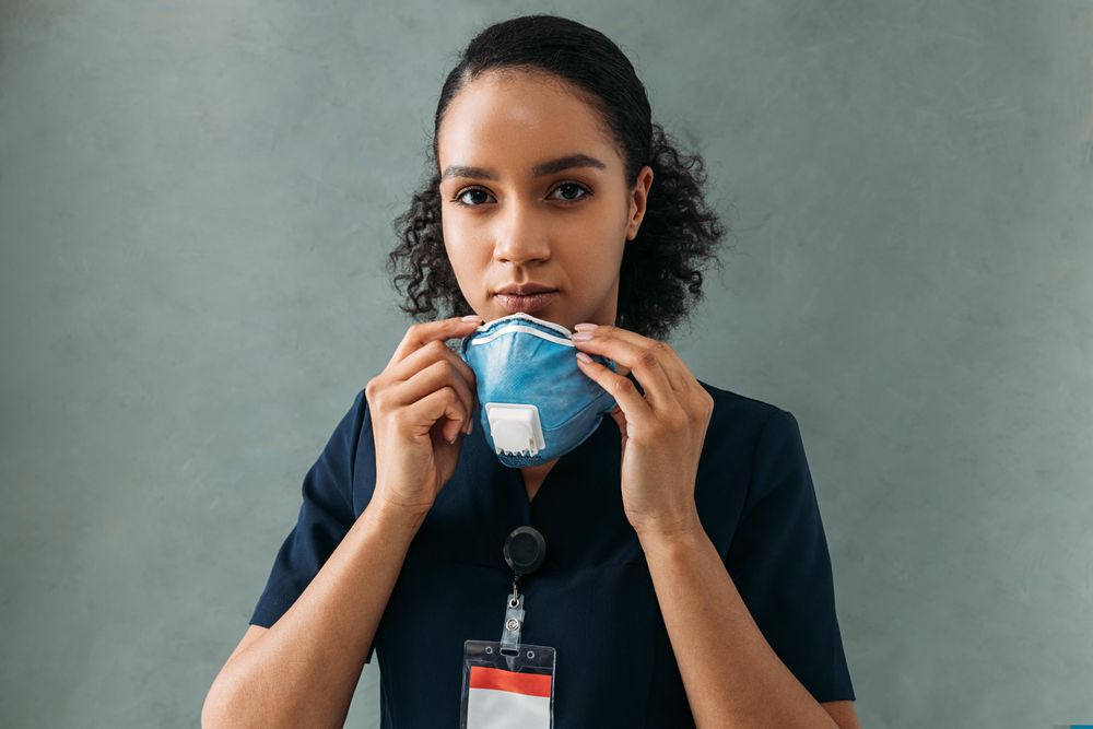 Black female doctor removing her face mask on grey background