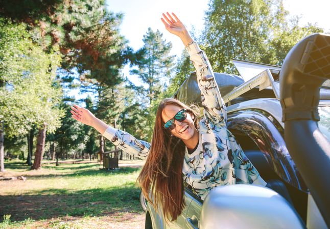 Happy woman raising arms through the window car