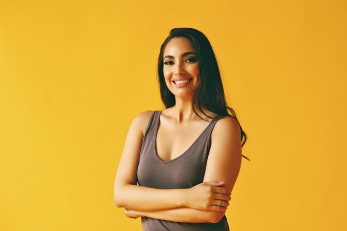 Confident smiling Hispanic woman standing and looking at camera in yellow room, copy space