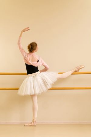 Ballerina practicing leg stretch at barre in dance studio.