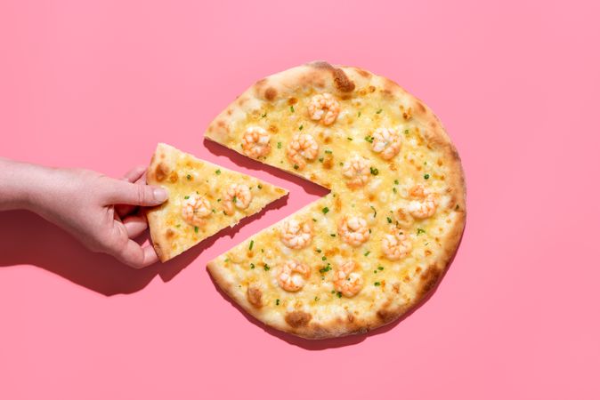 Shrimp pizza isolated on a pink background with hand taking a slice