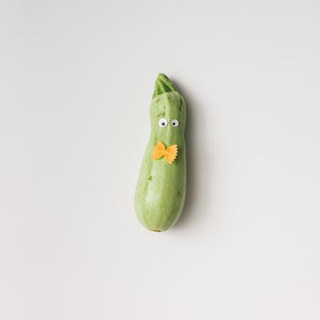 Zucchini with googly eyes and bowtie pasta on light background
