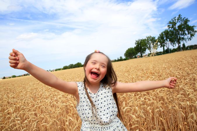 Happy girl with Down syndrome with outstretched arms in a wheat field