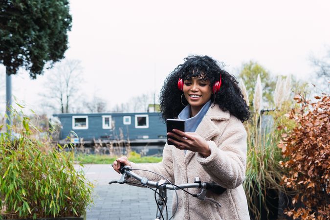 Delighted Black woman with smartphone on bicycle