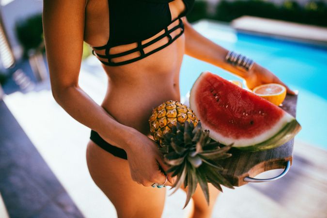 Woman in a bikini holding a fruit platter by the pool