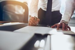 Close up of man in shirt and tie standing over desk and writing in sunny office