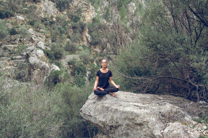 young meditating woman sitting on stone in Padmasana pose