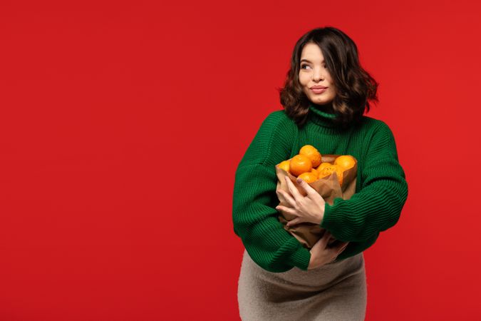 Woman holding paper bag full of fresh tangerines