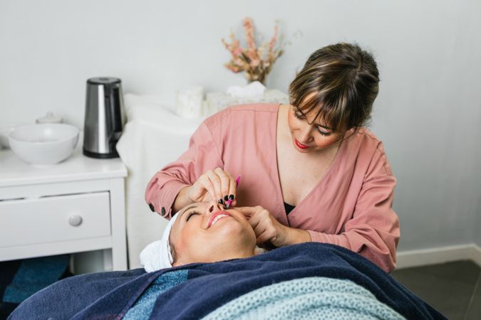 Beautician plucking eyebrows on face of woman in salon