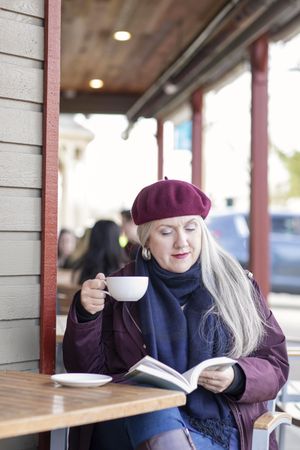 Mature woman reading a book and holding a cup of coffee