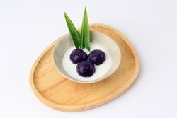 Bowl of 3 purple sweet potato balls covered in coconut milk sauce