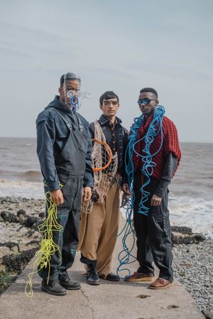 Three fishermen with nets and equipment standing on rocky shoreline