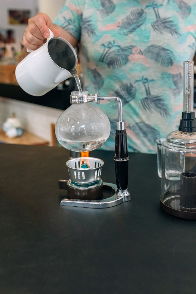 Unrecognizable barista skillfully preparing specialty coffee using Japanese siphon