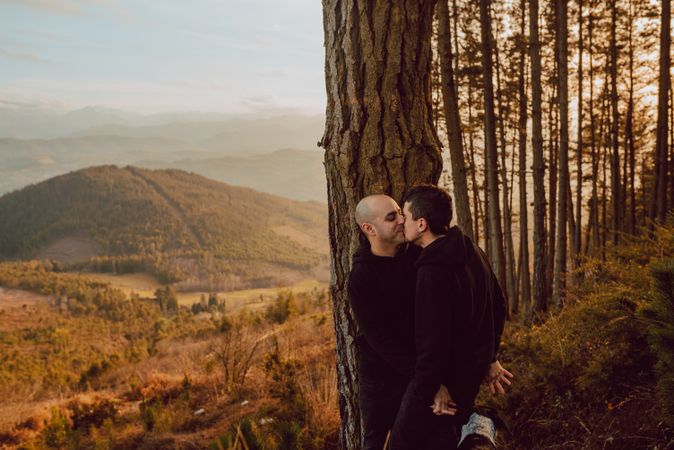 Smiling men hugging near tree in forest on hill