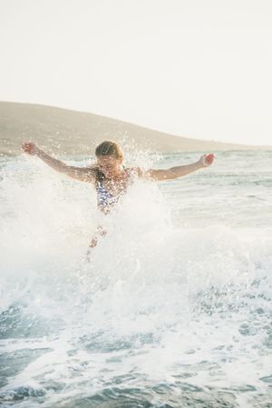 Woman with outstretched arms splashing in water at the beach