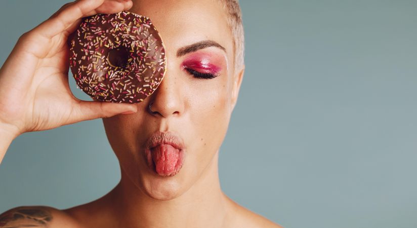 Female model a donut in front of her face on grey background