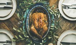Top view of centerpiece of roast chicken with decorative branches, with four plate settings
