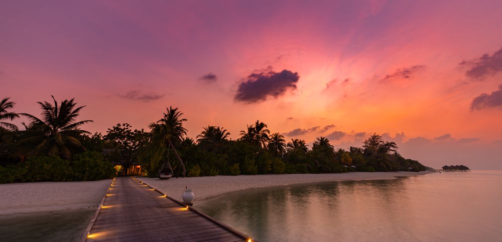 Wide shot of lit up walkway to a beach at a sunset