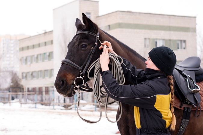 Person adjusting reins on saddled horse outdoors.