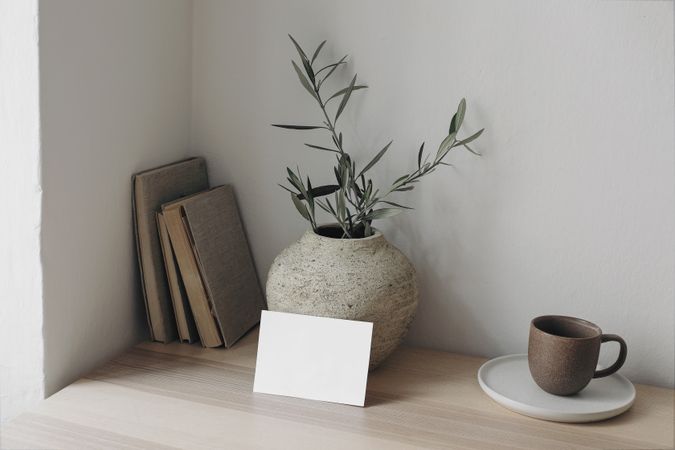 Wooden table with vase of eucalyptus branches, books and mug with mockup card