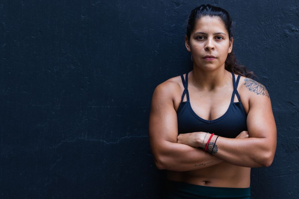 Hispanic sportswoman standing near wall