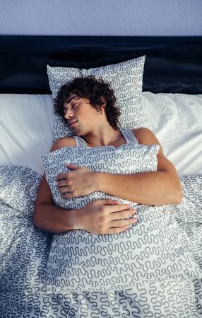 Man sleeping on his back in bed at home holding pillow