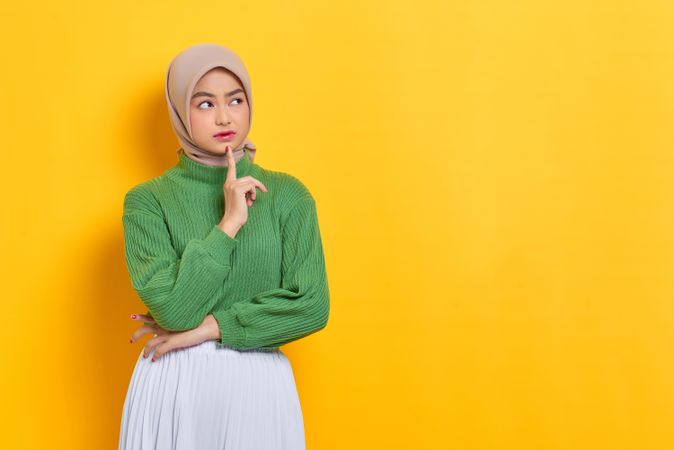Woman in headscarf wondering about something with finger on chin with copy space