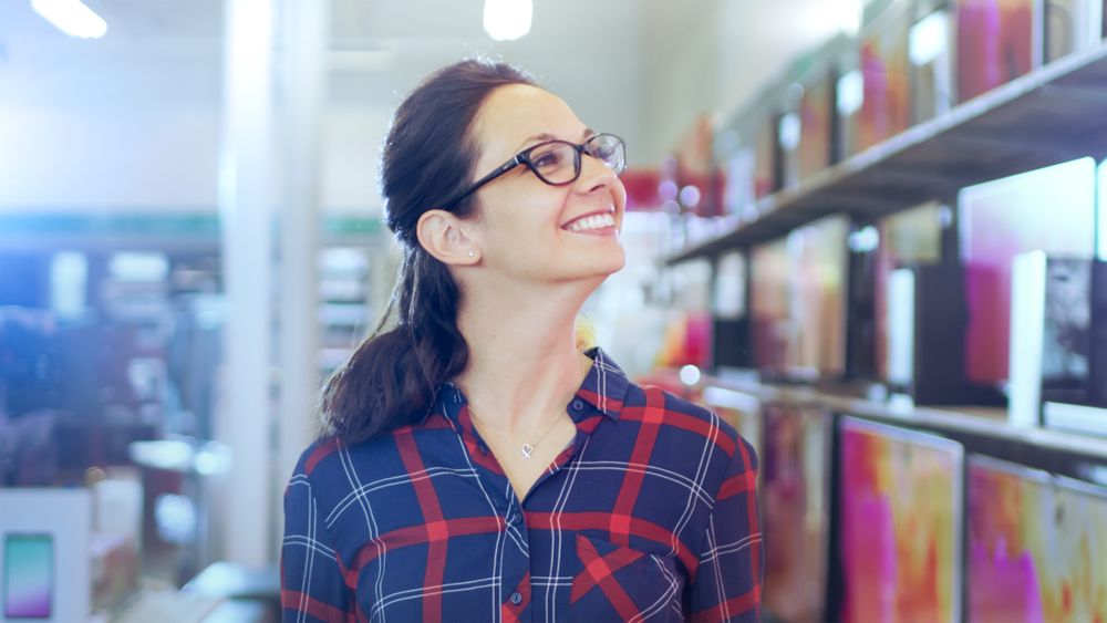 Beautiful Young Woman Walks In the Electronics Store Browsing Shelves with Latest Models of 4K UHD TV's.