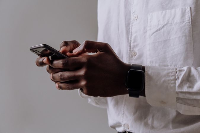 Cropped image of Black man in dress shirt holding smartphone