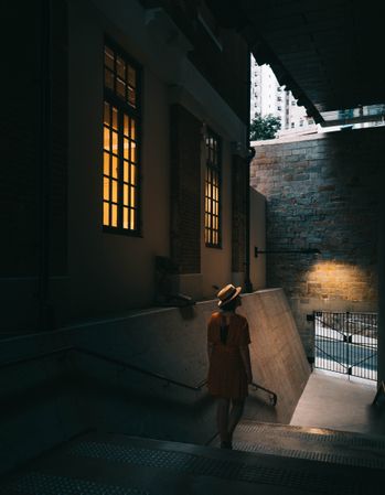 Back view of woman in yellow dress wearing a hat walking in an alley