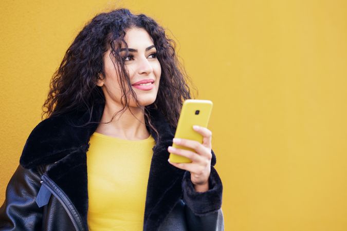 Smiling female standing with yellow phone in front of yellow background