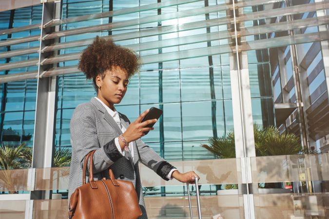 Traveling Black woman with baggage using smartphone on street