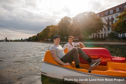 Two young male friends sitting in pedal boat and pedaling 5wqRLb