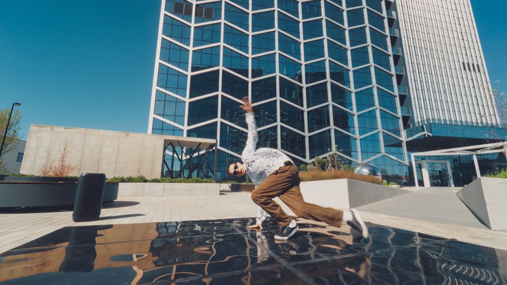 Outdoor Scene Capturing A Young Male Breakdancer Performing An Acrobatic Move In Plaza, With Reflective Surfaces