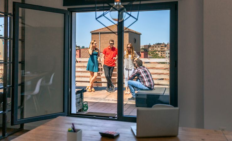View of teamwork talking in rooftop through a coworking office door