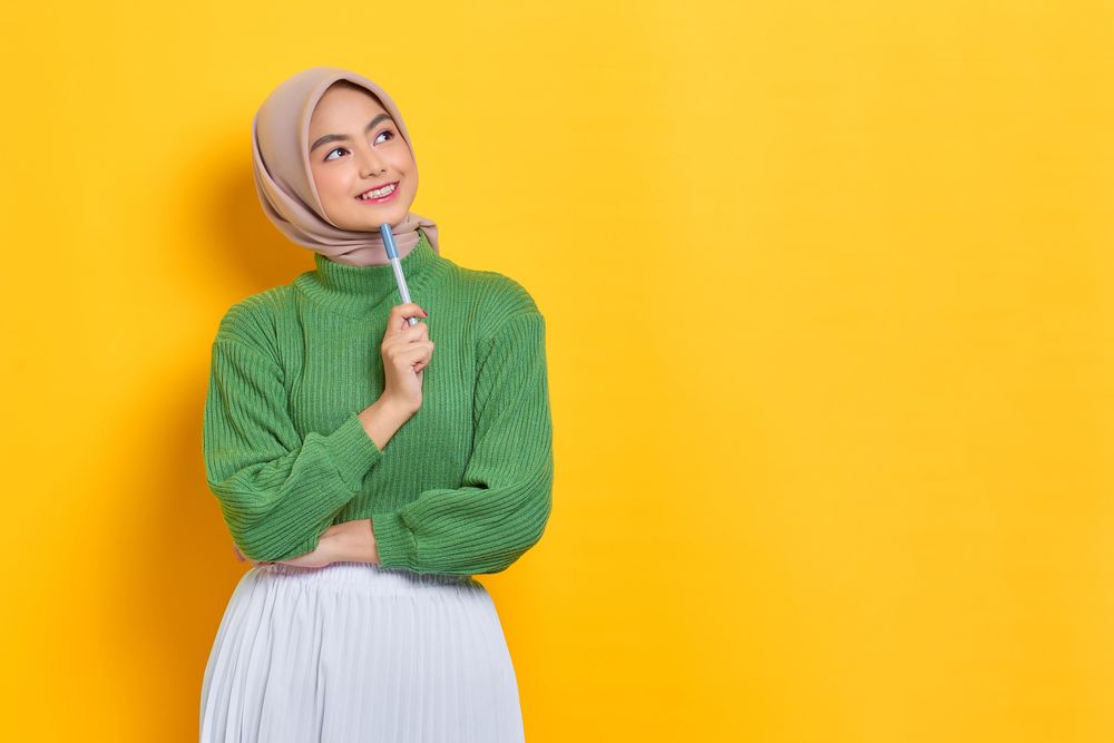 Smiling woman in headscarf looking to the side and thinking with pen