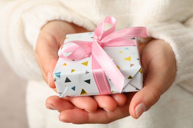 Woman in sweater holding gift box with pink bow, close up